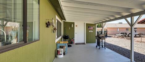 A covered outdoor area with a concrete floor, a grill, and a table with chairs.