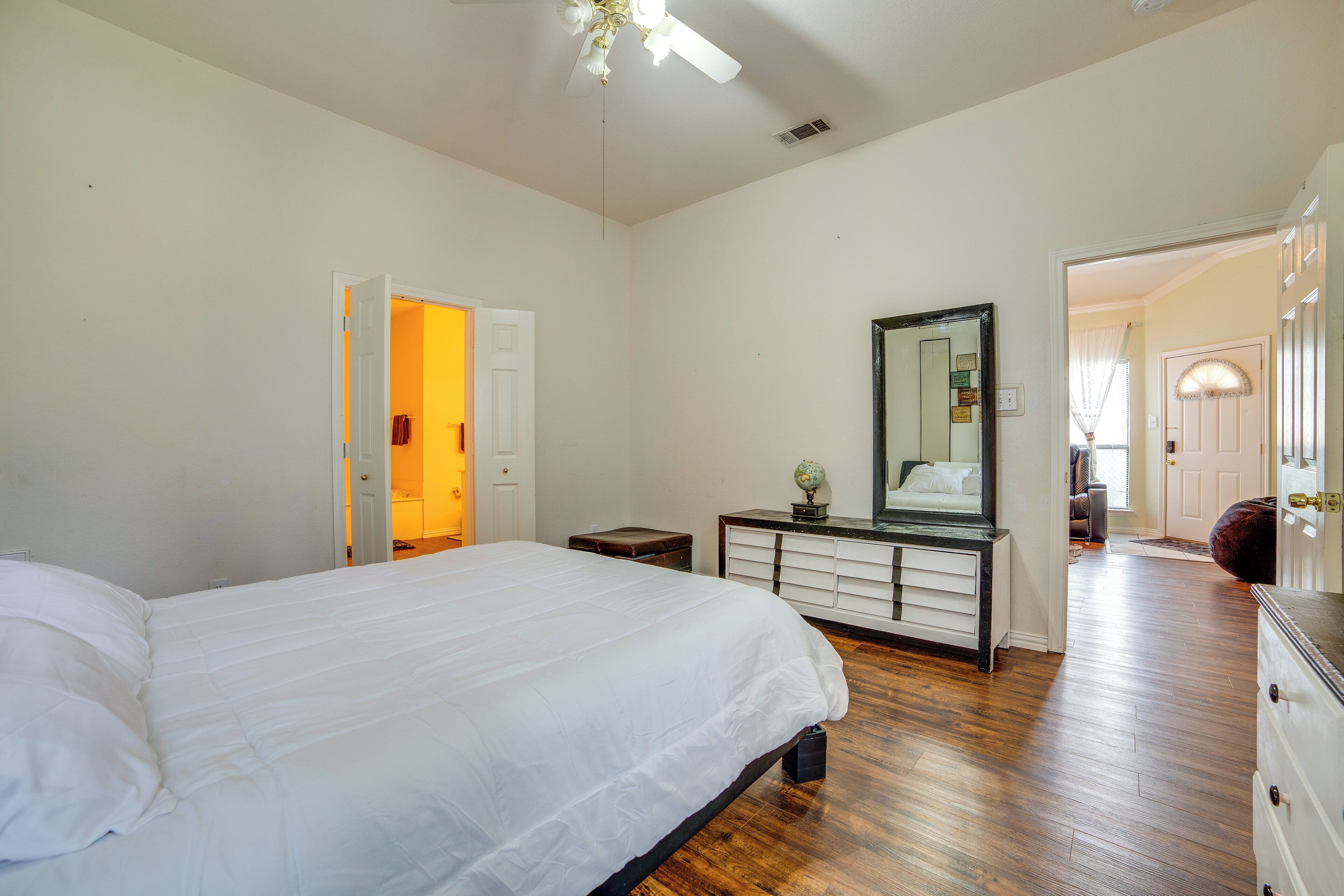 A bedroom with a large bed, a dresser, a mirror, and a door leading to another room.
