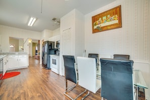 A modern kitchen with white cabinets, a red rug, and a dining area with black chairs and a glass table.