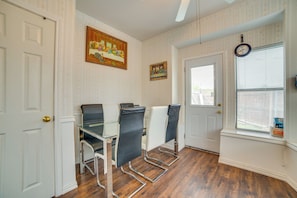 A dining area with a glass table and four chairs, a door, a window with blinds, and a wall-mounted clock.