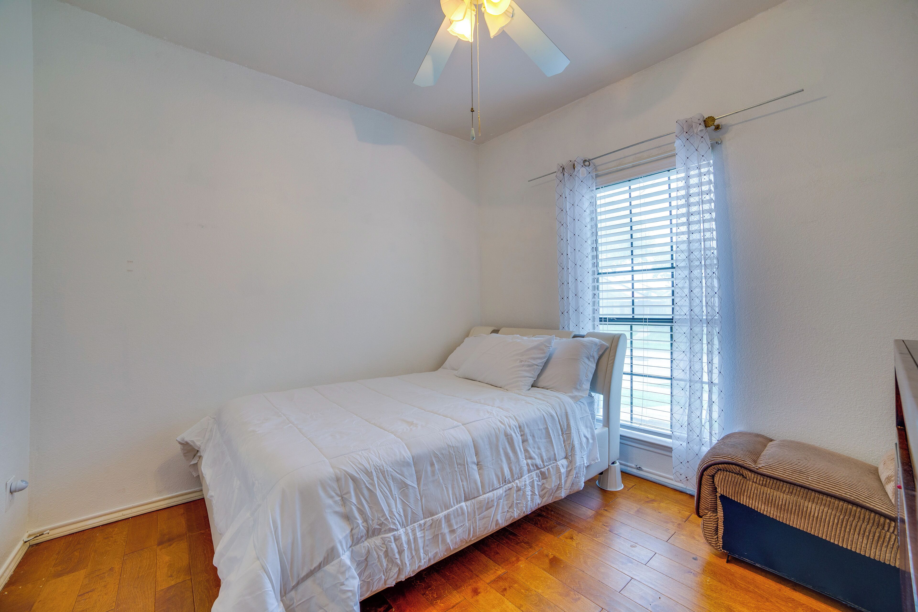Un dormitorio con cama, ventilador de techo, ventana con persianas y suelo de madera.