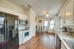 A kitchen with white cabinetry, a stainless steel refrigerator, a microwave, and a stove. There is a ceiling fan and a dining area with chairs and a table. - Extended DFW Retreat w/ Private Patio & Grill (Garland)