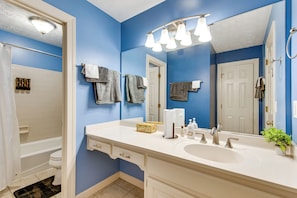 Un baño con pared azul, sanitarios blancos, un espejo grande y una zona de ducha.