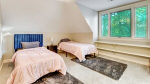 Een slaapkamer met twee bedden, een plafondventilator, een groot raam met uitzicht op bomen, en een ingebouwde bank.