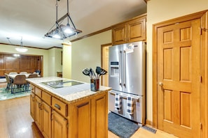 Una cocina con armarios de madera, un refrigerador de acero inoxidable, encimera de granito y un comedor con sillas.