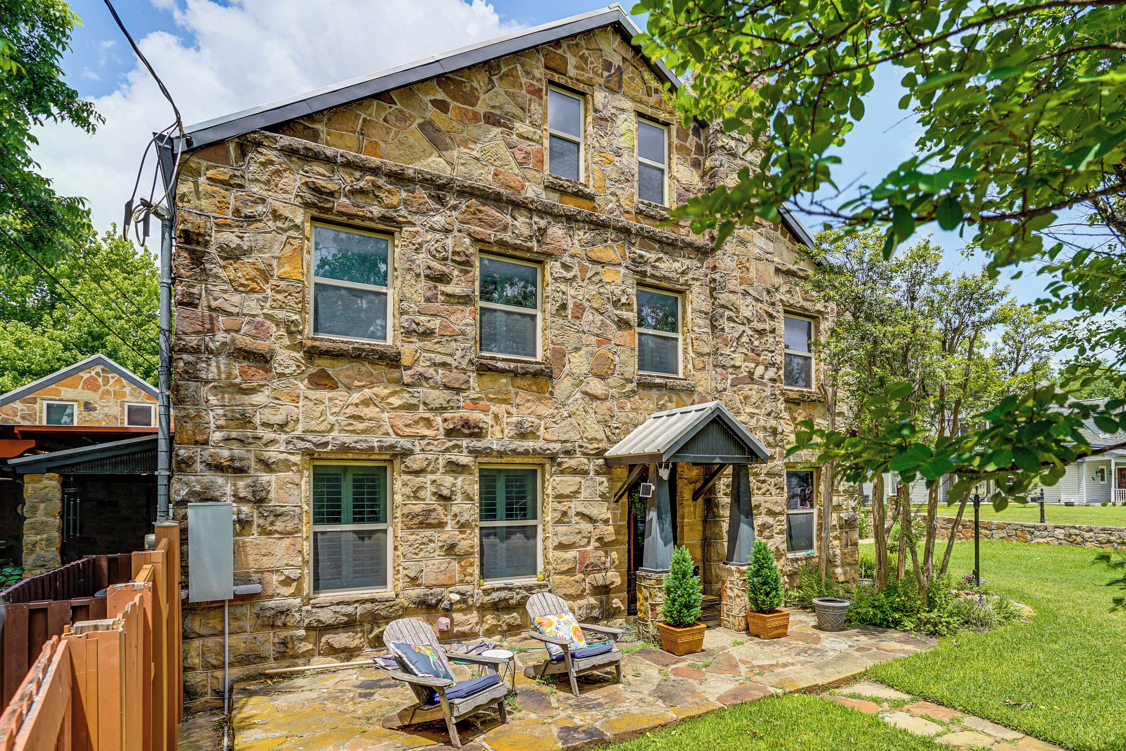 A stone building with multiple windows, a covered porch, and outdoor seating.