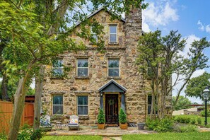 A stone house with a front porch, a wooden fence, and a lawn. - Historic Weatherford Estate w/ Backyard Oasis (Weatherford)