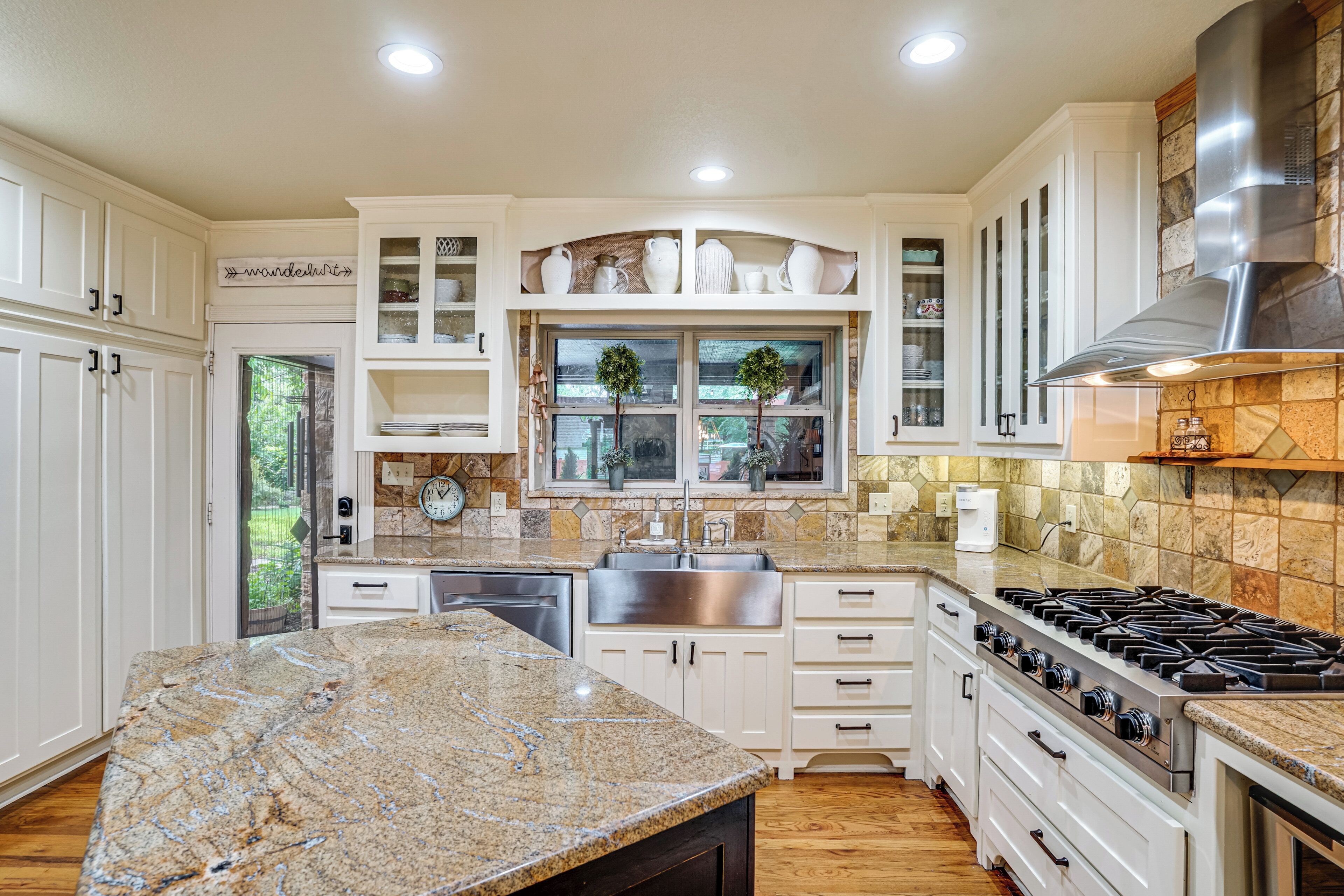 A kitchen with white cabinets, a granite countertop, a stainless steel sink, and a gas stove.