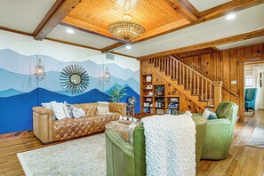 A living room with a wooden staircase, a blue mural, a brown leather sofa, and a green armchair. - Historic Weatherford Estate w/ Backyard Oasis (Weatherford)