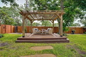 A wooden pergola with a table and chairs underneath, surrounded by a grassy yard.