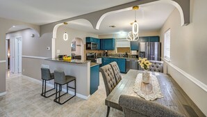 A modern kitchen with blue cabinets, a central island, and a dining area with a table and chairs. - Golf, Beaches & Sunshine! Pet-friendly Naples Home (Naples)