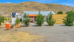 Una caravana con la etiqueta 'Forest River', un pequeño edificio con techo rojo y una valla de madera en un entorno rural con montañas al fondo.
