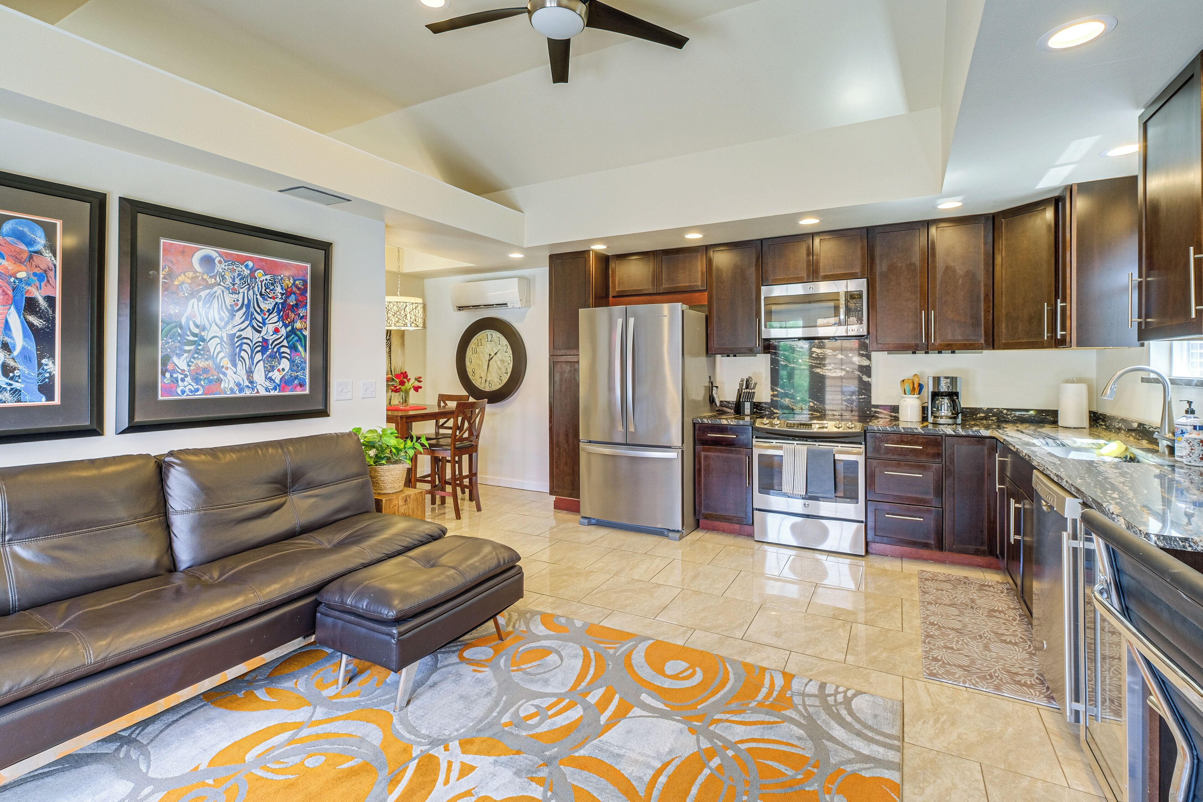A modern kitchen with dark wood cabinets, stainless steel appliances, and a dining area with a leather sofa and a patterned rug.