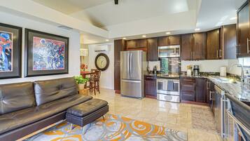 A modern kitchen with dark wood cabinets, stainless steel appliances, and a dining area with a leather sofa and a patterned rug.