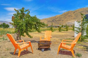 An outdoor seating area with two orange chairs and a fire pit, surrounded by a natural landscape with hills and a clear sky. - Walk to River + Bike Trail! East Wenatchee Escape (East Wenatchee)