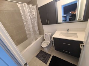 A bathroom with a shower, toilet, sink, and dark cabinets.