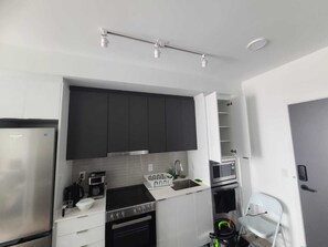 Cocina compacta con refrigerador, estufa, microondas y un lavamanos pequeño.