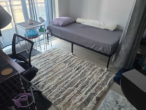 Un dormitorio con una cama, un escritorio, una silla y una mesita de noche con un reloj.