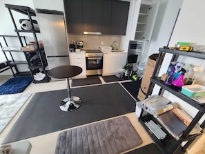 A compact kitchen with modern appliances, a small dining area, and a storage shelf with cleaning supplies.