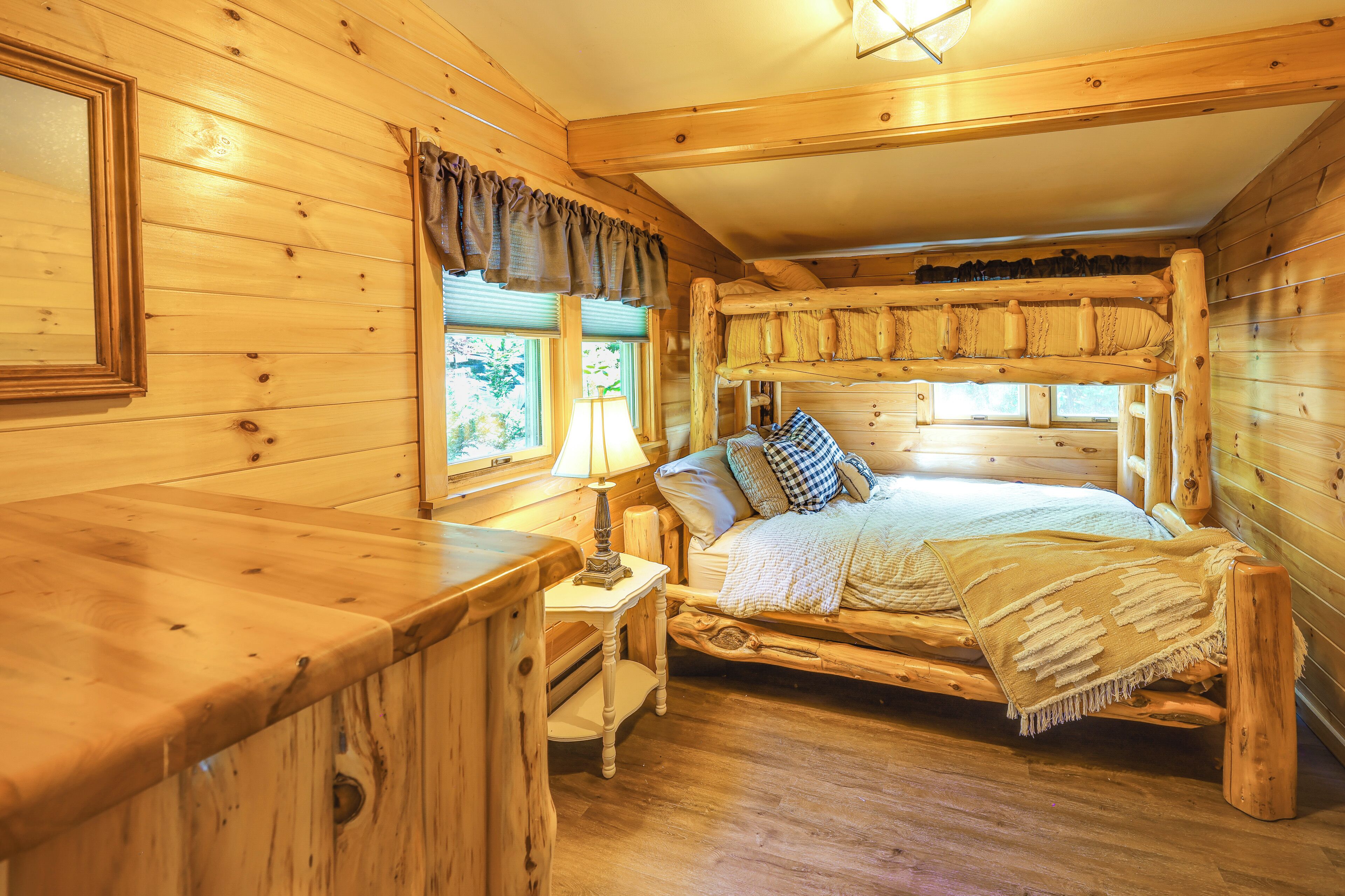 A wooden cabin bedroom with a bunk bed, a bedside table with a lamp, and a window with curtains.