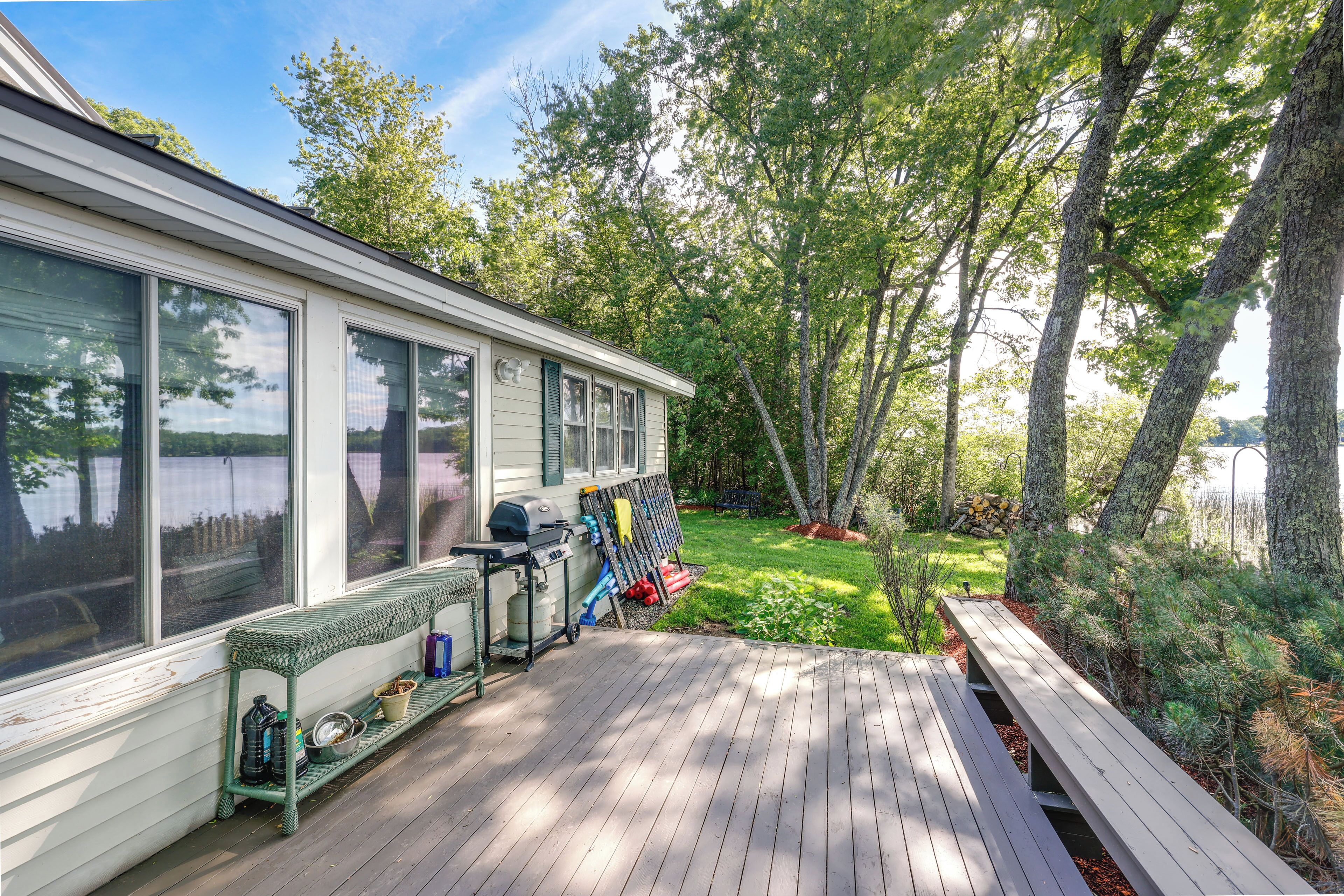 A wooden deck with a bench and a grill, surrounded by trees and a grassy area.