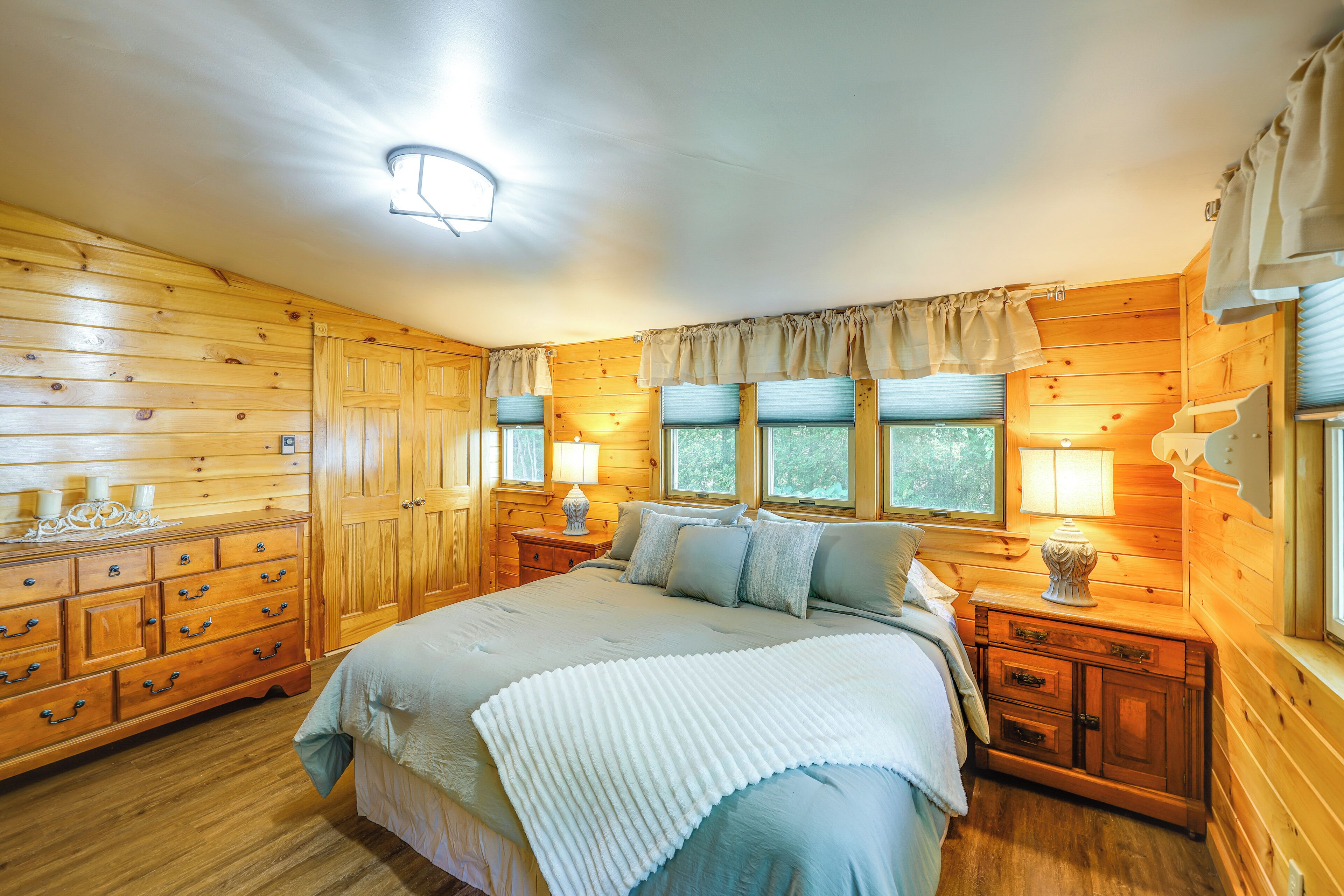 Une chambre dans une cabane en bois, avec un lit, une commode, des tables de chevet et des fenêtres.