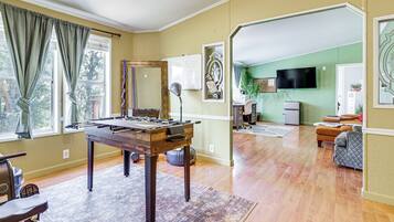 A living room with a foosball table, a sofa, a television, and a dining area with a table and chairs.