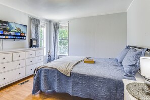 Ein Schlafzimmer mit Bett, Fernseher an der Wand, Kommode und einem Fenster mit Vorhängen.