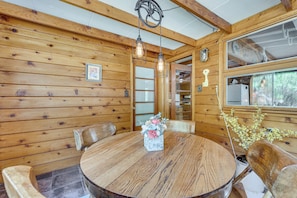 A wooden interior with a round dining table, chairs, hanging light fixtures, and a window with a view. - On-site Fishing! Riverfront Gem w/ Patios in Drake (Drake)
