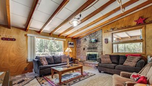 A cozy living room with a fireplace, wooden beams, and a stone wall. - On-site Fishing! Riverfront Gem w/ Patios in Drake (Drake)
