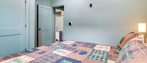Un dormitorio con colcha acolchada, una lámpara de noche y una puerta que da a otra habitación.