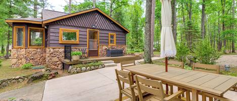 A cabin with a stone foundation, wooden exterior, and a patio with a table and chairs.