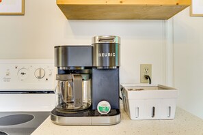 Eine Kaffeemaschine von Keurig steht auf einer Küchenarbeitsplatte, zusammen mit einem Kapselhalter und einer Steckdose.