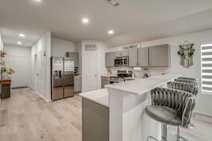 A modern kitchen with grey cabinets, stainless steel appliances, and a white countertop.