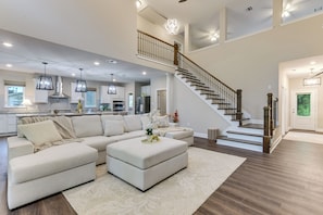 A spacious living area with a large sectional sofa, a coffee table, and a staircase leading to an upper level. - On Several Acres! Luxury Home in Prairieville (Prairieville)