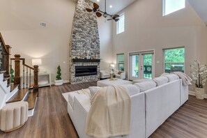 A spacious living room with a stone fireplace, a large white sofa, and a wooden staircase. - On Several Acres! Luxury Home in Prairieville (Prairieville)