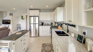 Una cocina moderna con armarios blancos, electrodomésticos de acero inoxidable, encimera de granito y un reloj digital.