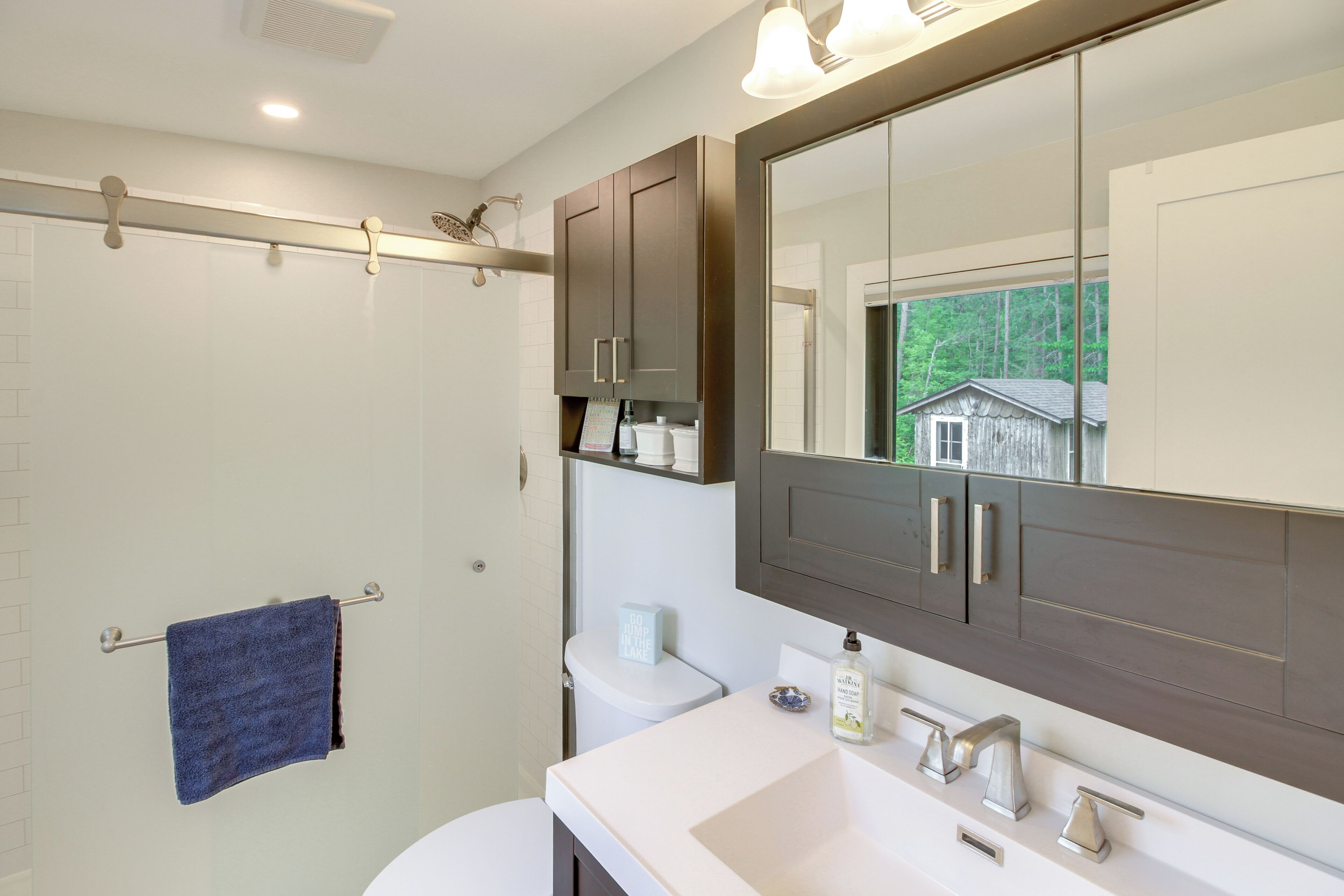 A bathroom with a large mirror, white sink, and dark cabinets.