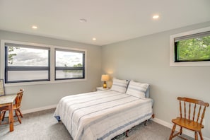 Un dormitorio con cama, dos ventanas, escritorio, silla y lámpara.