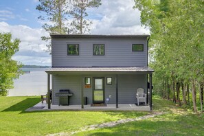 Una casa de dos pisos con un porche cubierto, una parrilla y una silla afuera.