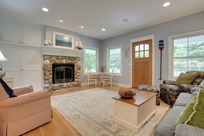 A living room with a stone fireplace, a sofa, a coffee table, and a view of the outdoors through large windows. - South Haven Family Lake Getaway 4 Mi to Downtown (South Haven)