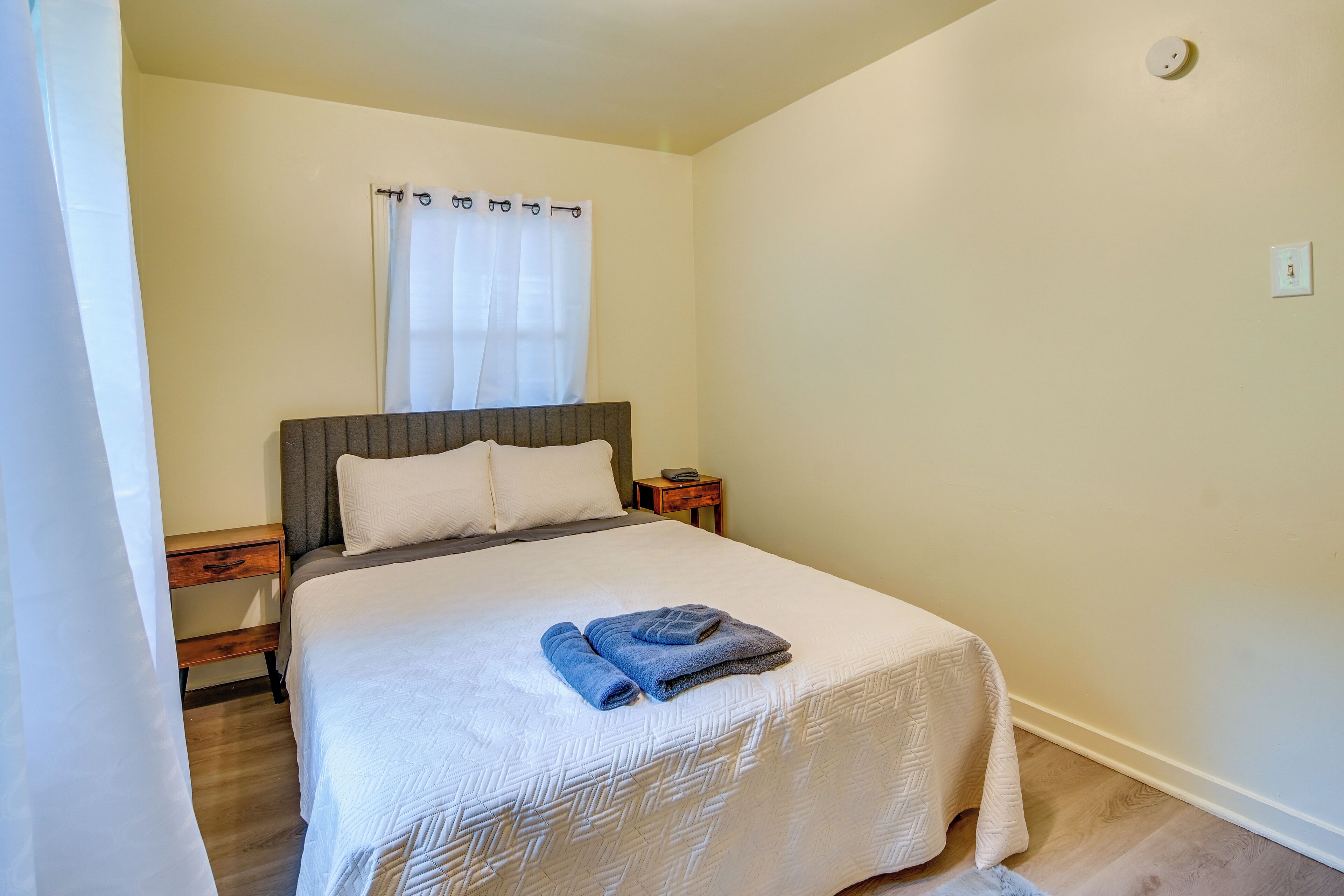 Une chambre à coucher avec un lit, une table de chevet, une commode et une fenêtre avec des rideaux.