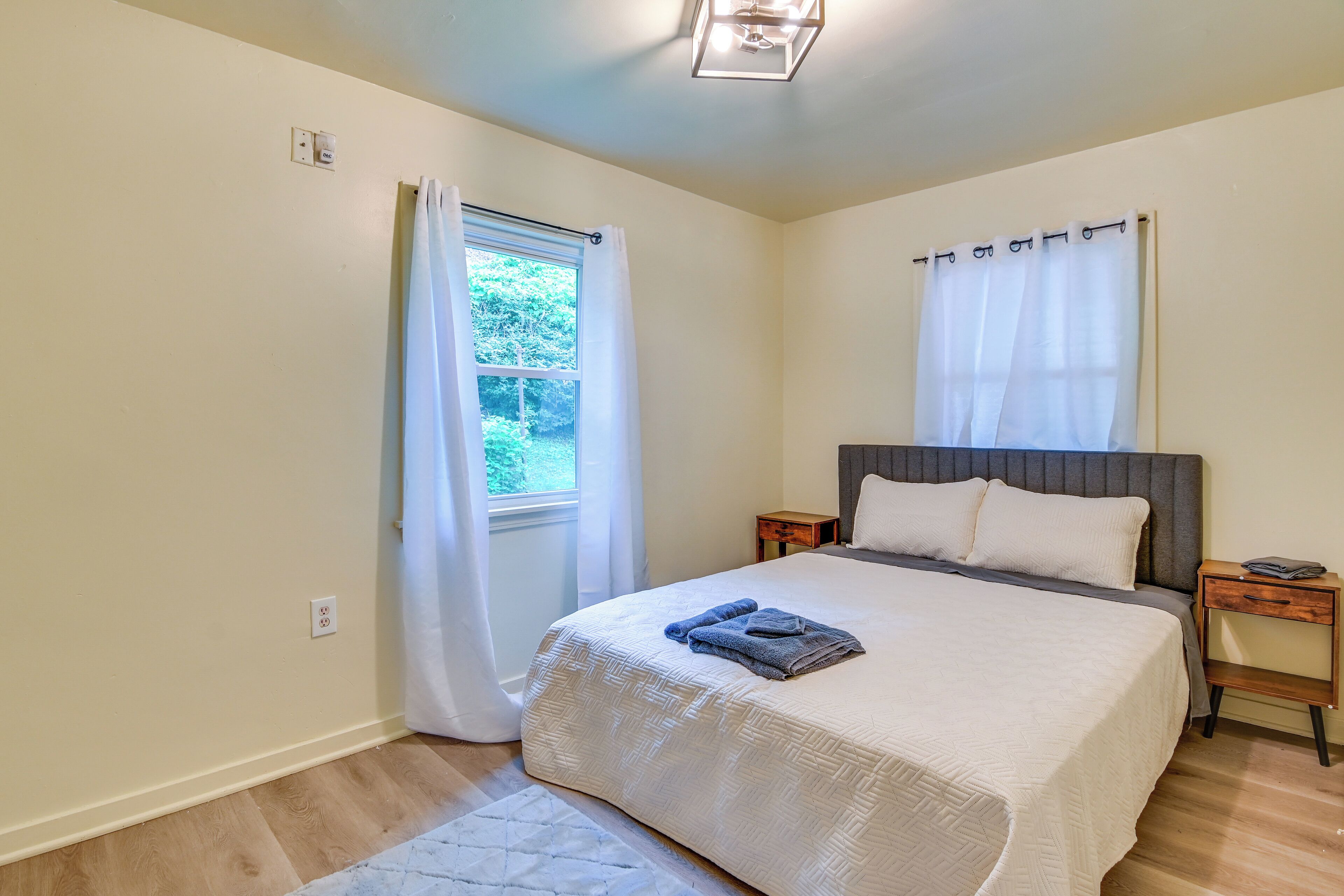 A bedroom with a bed, a nightstand, a window with curtains, and a light fixture.