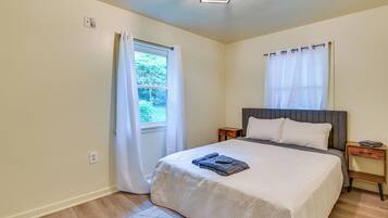 A bedroom with a bed, a nightstand, a window with curtains, and a light fixture.