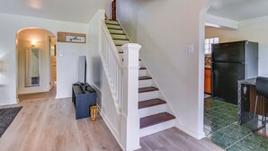 Una escalera que lleva al segundo piso, un área de cocina con un refrigerador, y un letrero en la pared que dice 'gather'.
