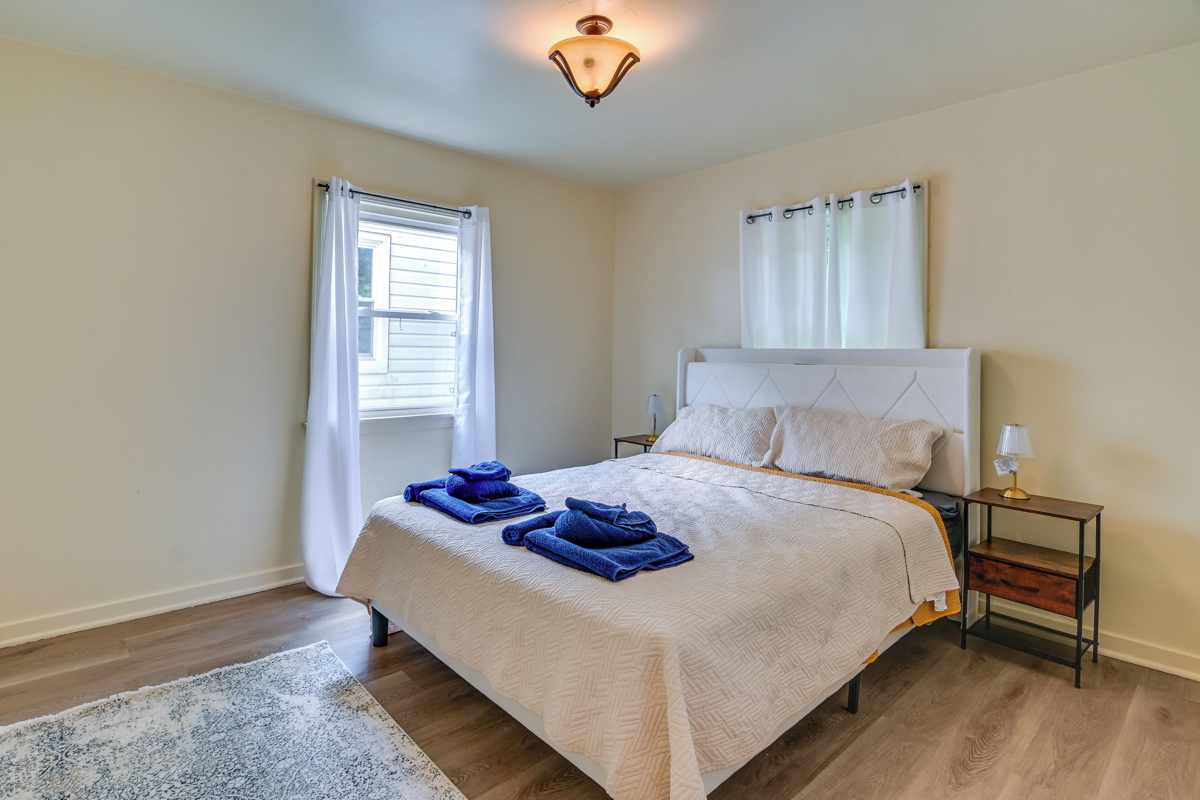 A bedroom with a bed, a nightstand, a lamp, a window with curtains, and a rug.