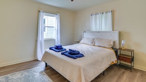Un dormitorio con cama, mesita de noche, lámpara, ventana con cortinas y alfombra.