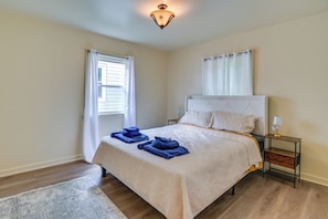 Un dormitorio con cama, mesita de noche, lámpara, ventana con cortinas y alfombra.