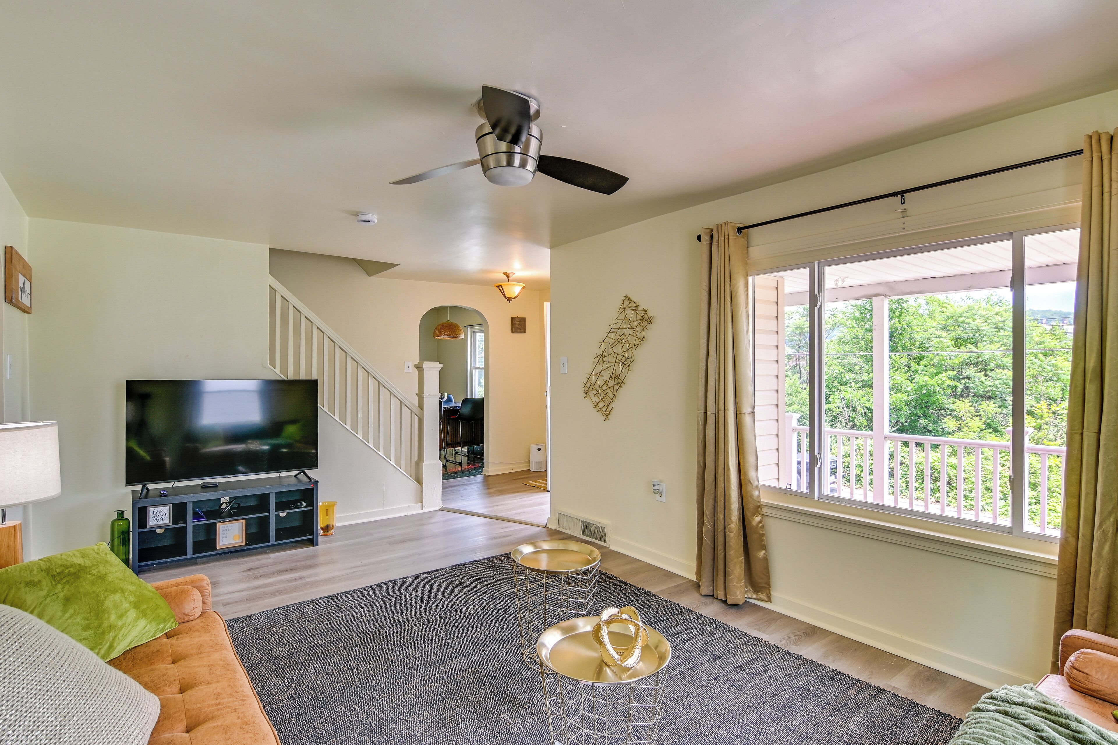 A living room with a TV, a staircase, and a balcony with curtains.