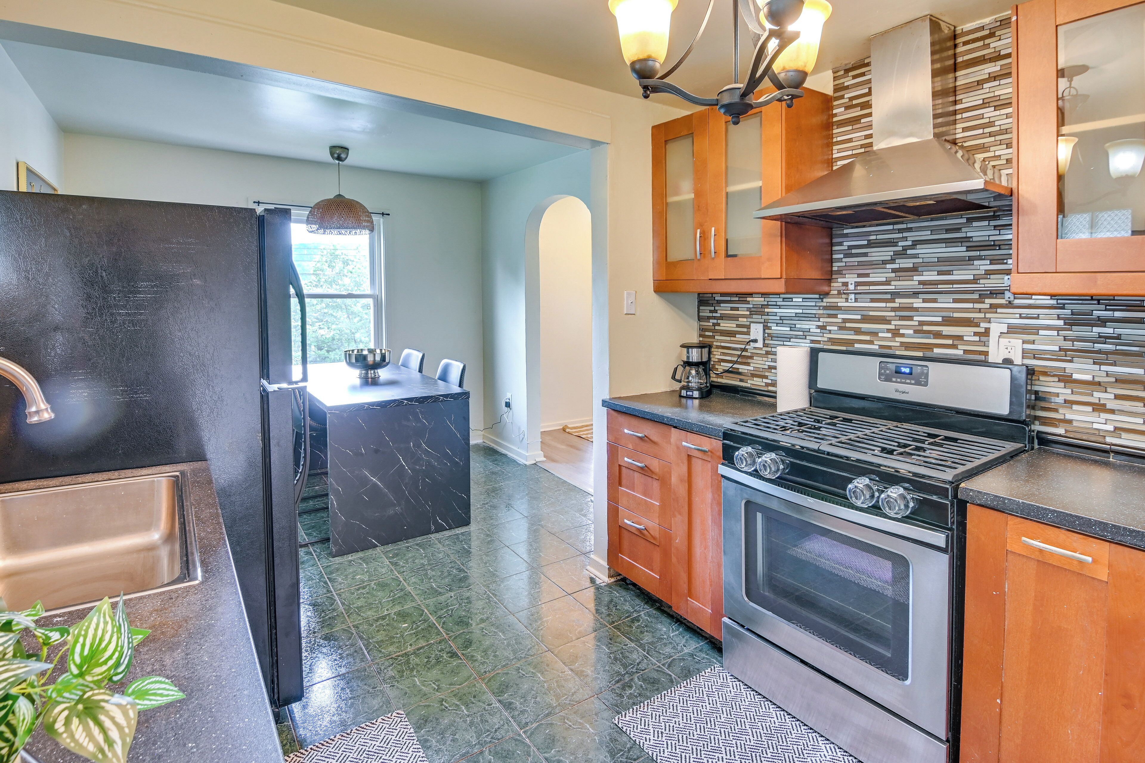 A kitchen with a stainless steel refrigerator, a stove, wooden cabinets, and a tiled backsplash.